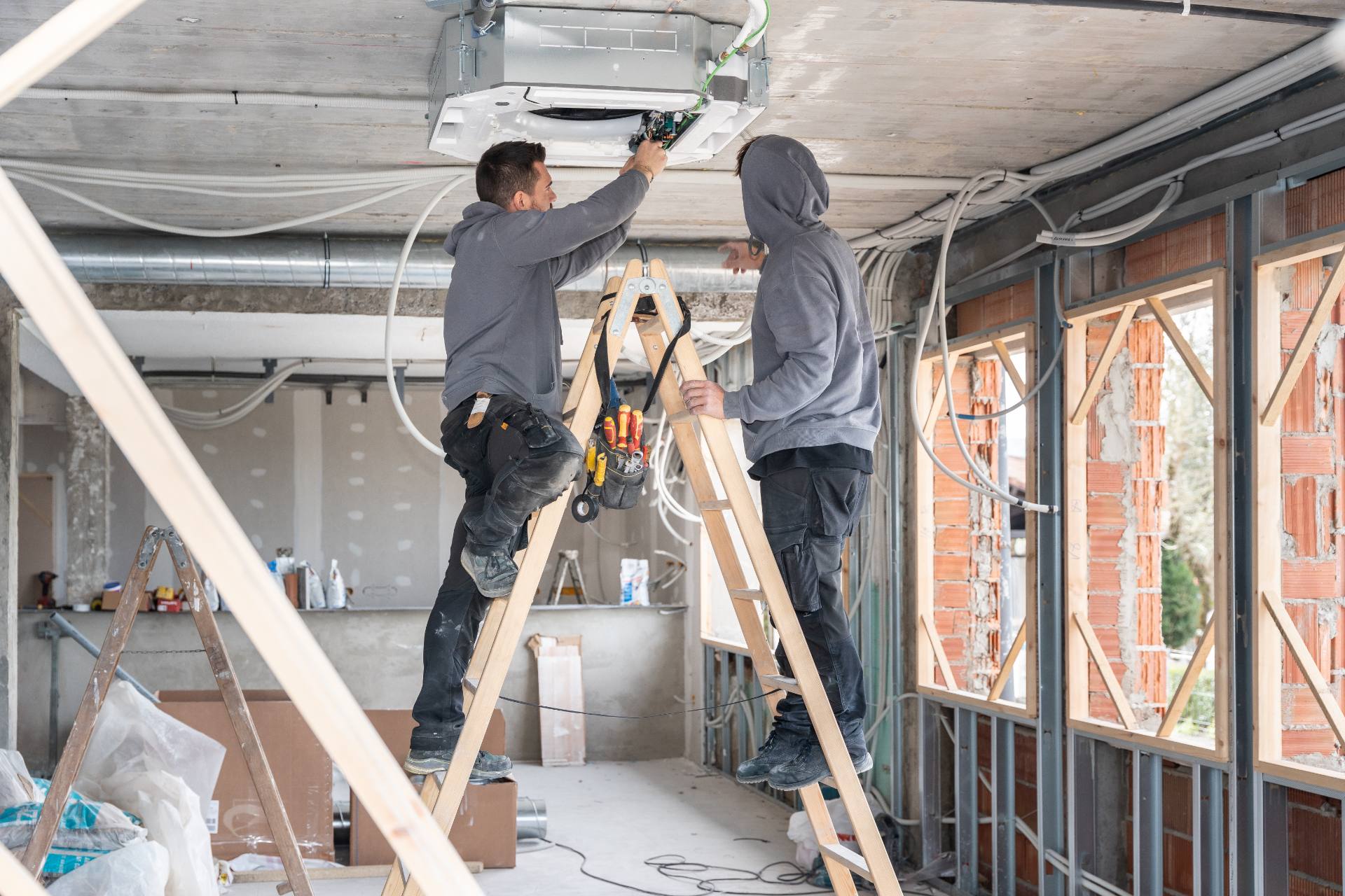 Electricians installing ceiling unit on site